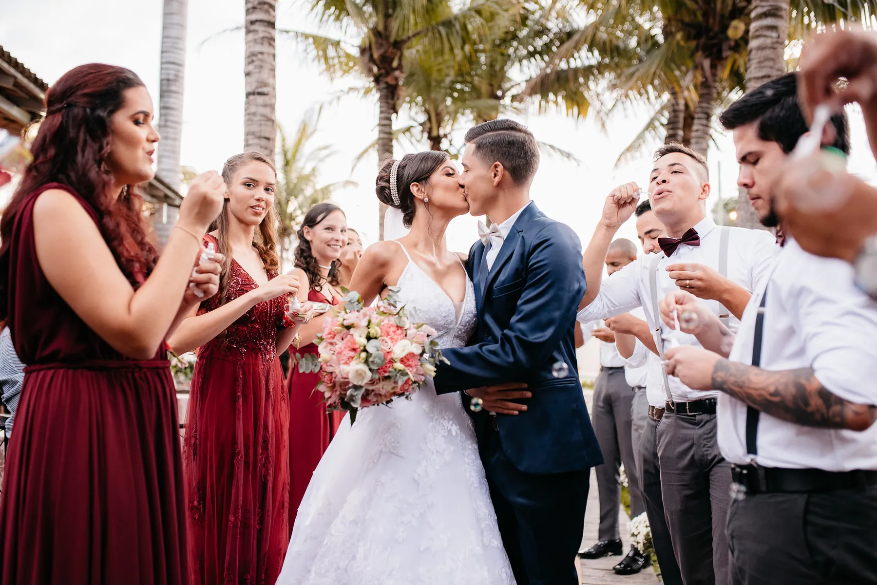 Noivos se beijando com padrinhos comemorando em casamento